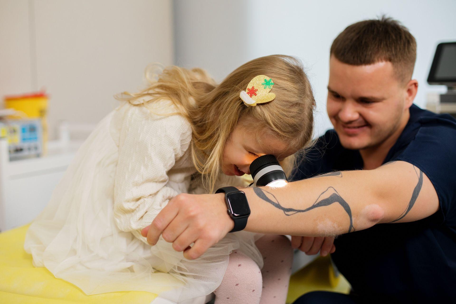 Дитина оглядає шкіру лікаря під дерматоскопом